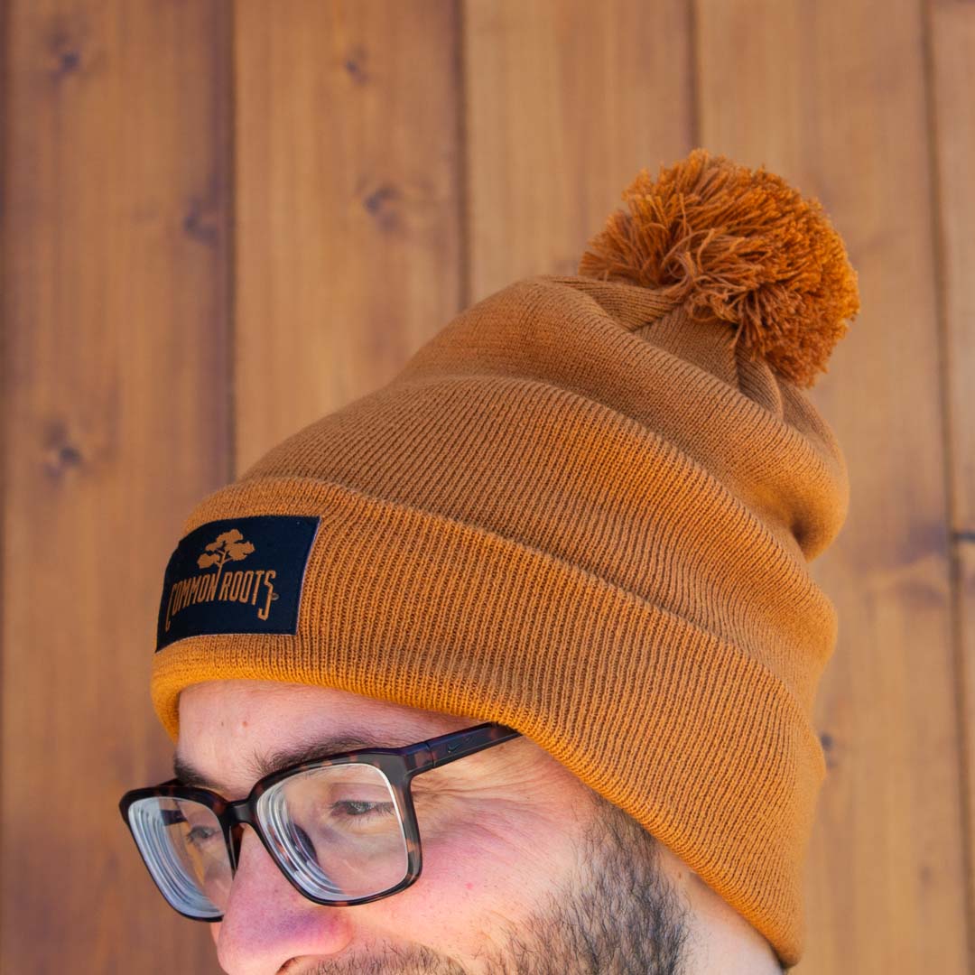 Rust colored beanie with black common roots patch and pom pom