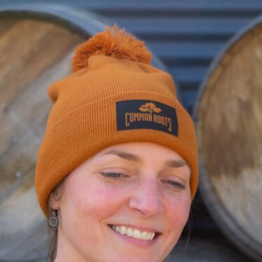 Rust colored beanie with black common roots patch and pom pom