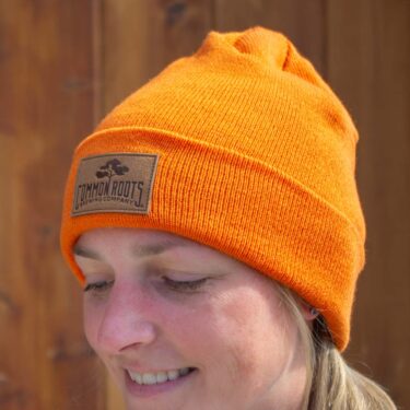 Woman wearing bright orange beanie with leather patch on it