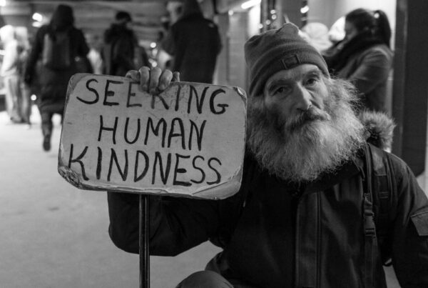 Homeless man holding a sign that reads "seeking human kindness"