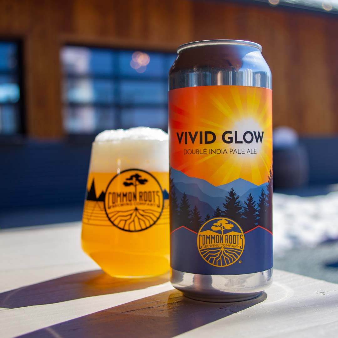 Can of Vivid Glow casting a shadow in bright sunlight, sitting next to a glass of vibrant beer