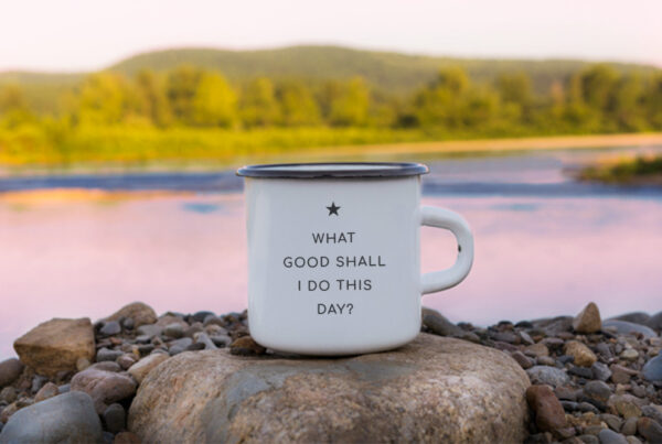 Tin coffee mug in front of a lake that reads, "What good shall I do this day."