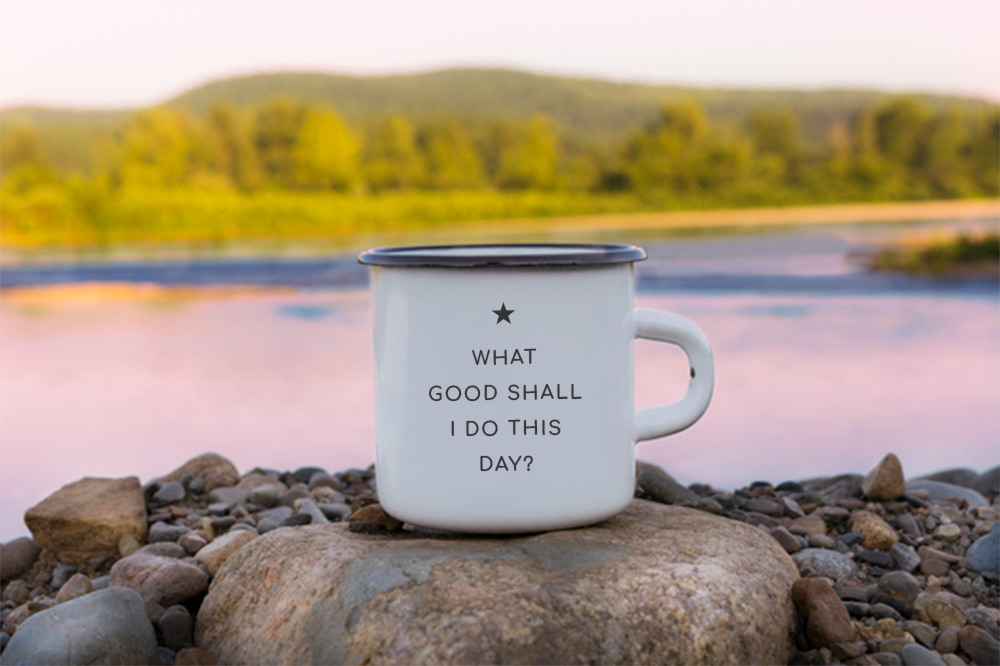 Tin coffee mug in front of a lake that reads, "What good shall I do this day."