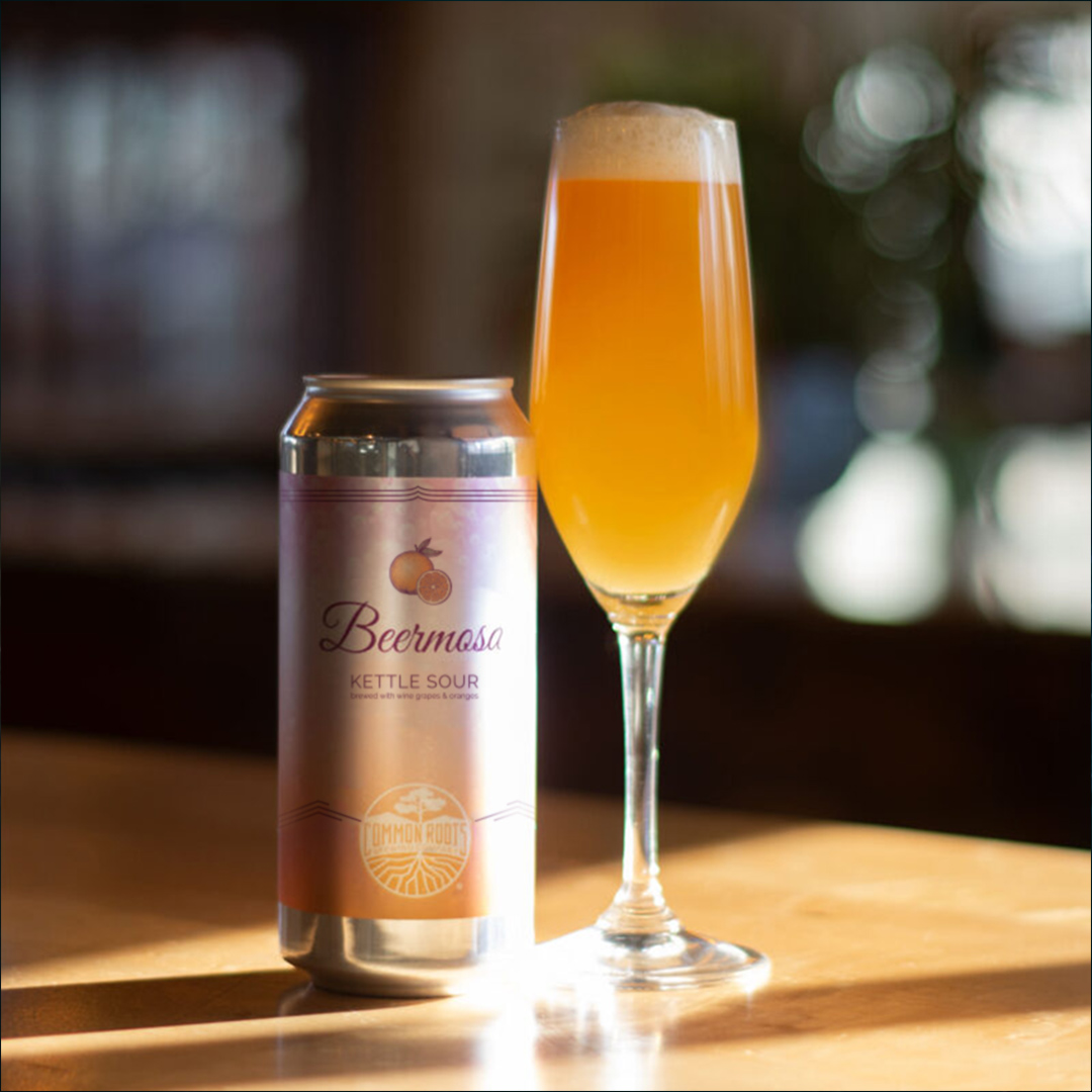 Can of Beermosa next to a champagne glass of frothy beer