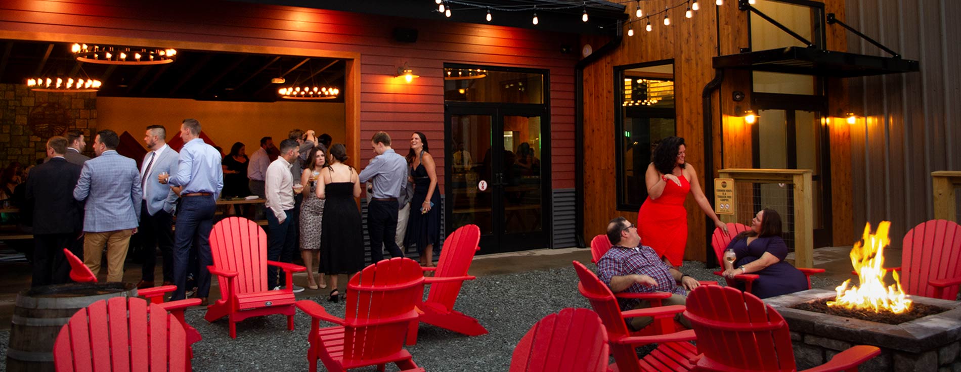 People in wedding attire gathered socially with fire pits and twinkling lights