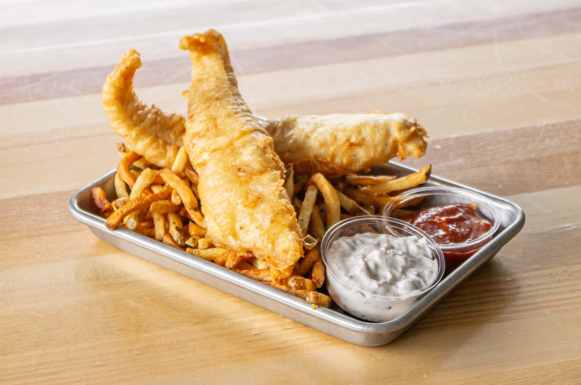 Two pieces of perfectly fried fish on a bed of french fries with side sauces.