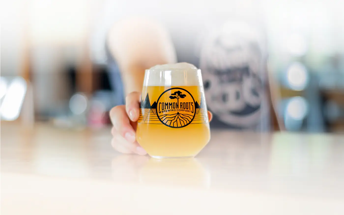 Person pushing a glass of hazy beer toward the camera