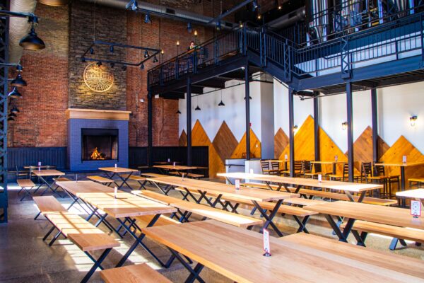 Large room with massive stone fireplace, brick walls, and long wooden tables