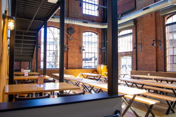 Large room with brick walls, tall windows, and long wooden tables