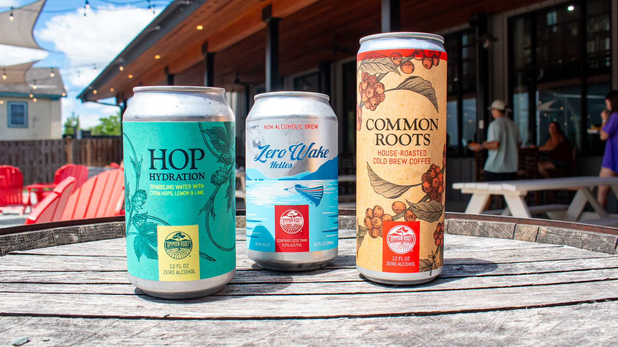 Cans of Hop Hydration, Zero Wake, and Common Roots Cold Brew lined up on a barrel in the beergarten