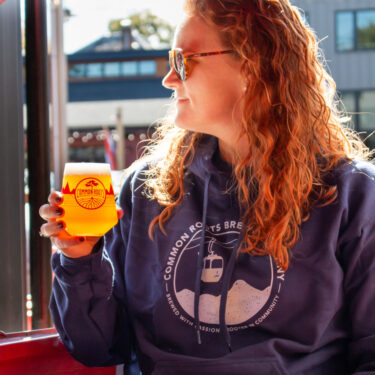 Woman wearing the Gondola sweatshirt, holding a beer.