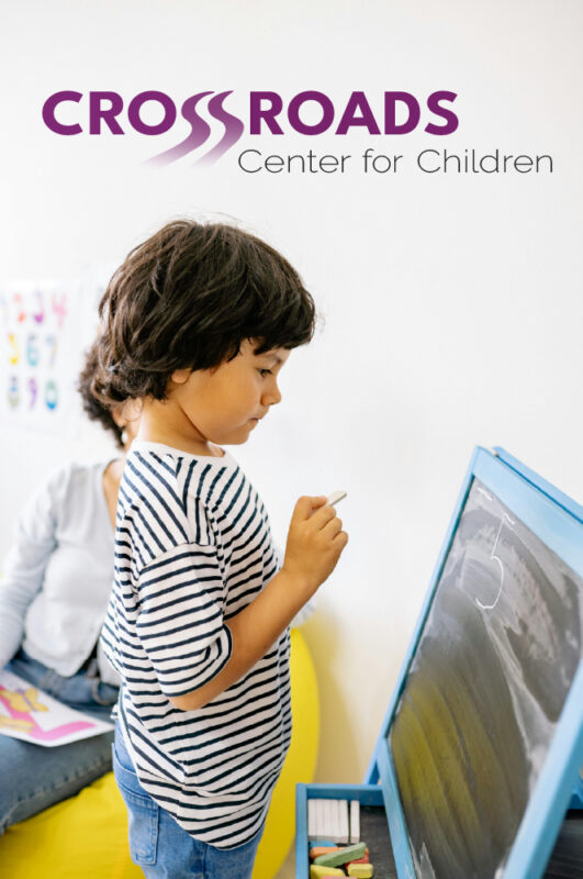 Child drawing on a chalkboard with Crossroads Center Logo